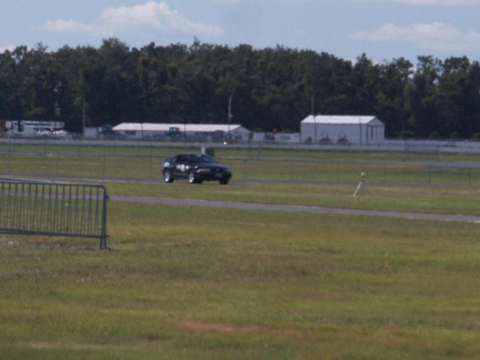 2001 Mercury Grand Marquis driving on a racetrack with trees and buildings in the background