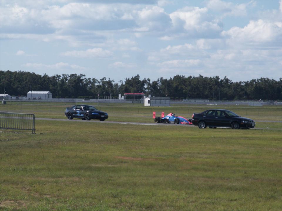 Race car with blue and pink livery on track with two sedans