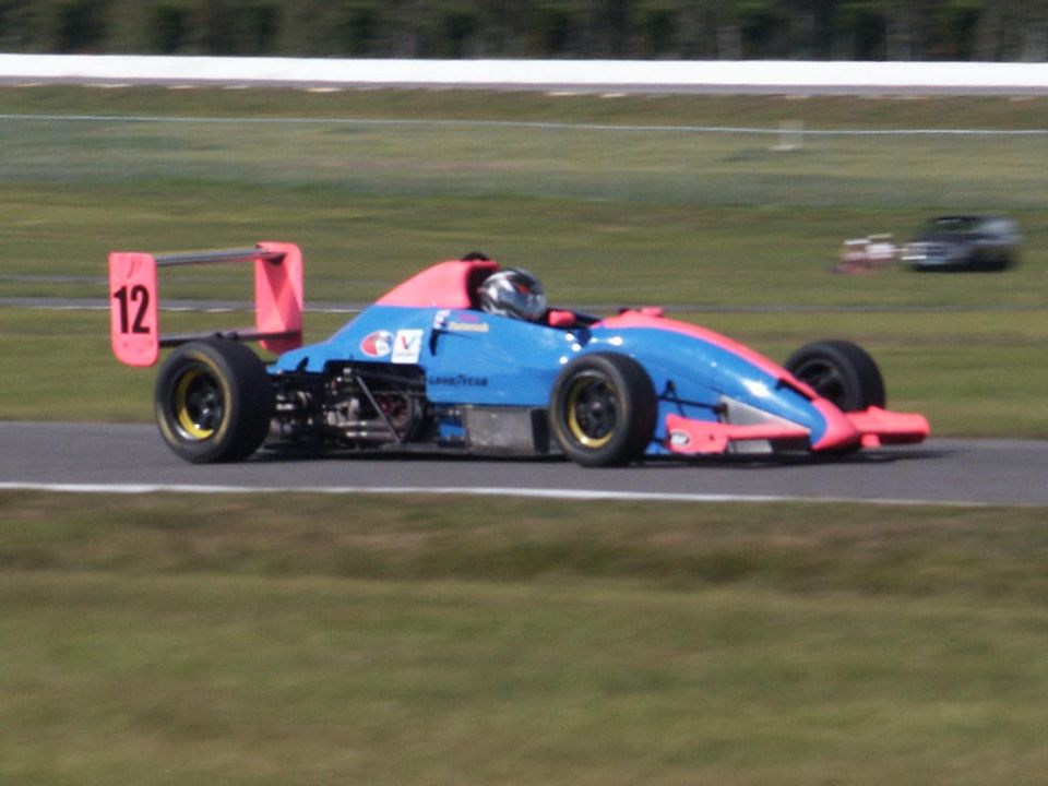 Race car with blue and pink body, number 12 on the rear wing, on a track