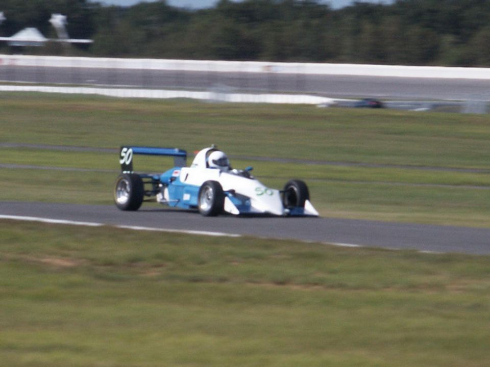 Blue and white number 50 open-wheel formula car cornering on a road course