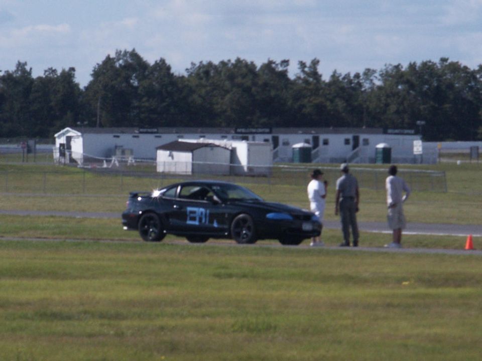 Black coupe with racing numbers '381' on the door, parked on a track with people standing nearby