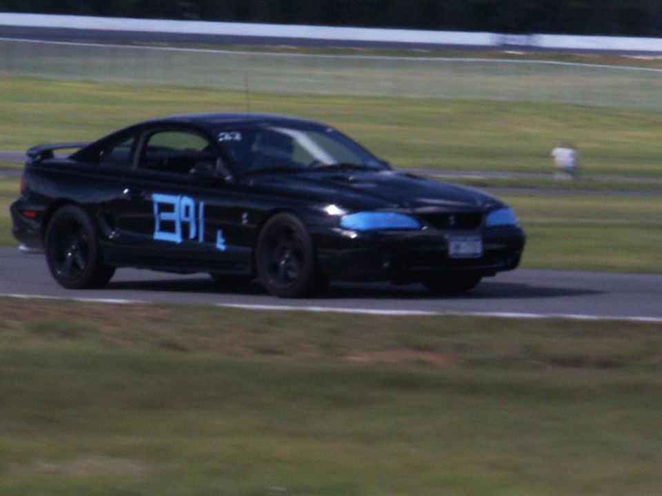 Black Ford Mustang with blue numbers '391' on the side, driving on a race track