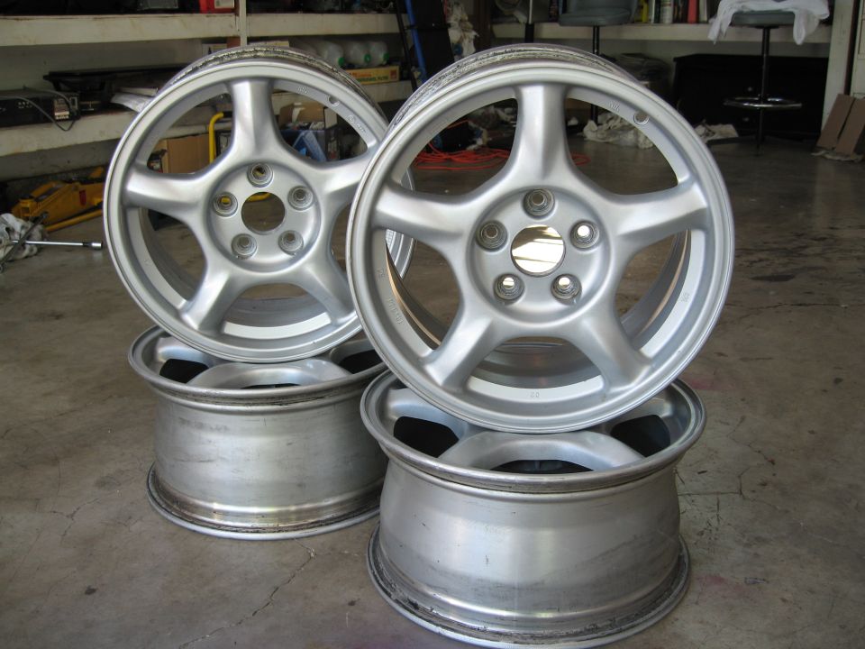 Four silver 5-spoke alloy wheels stacked in a garage