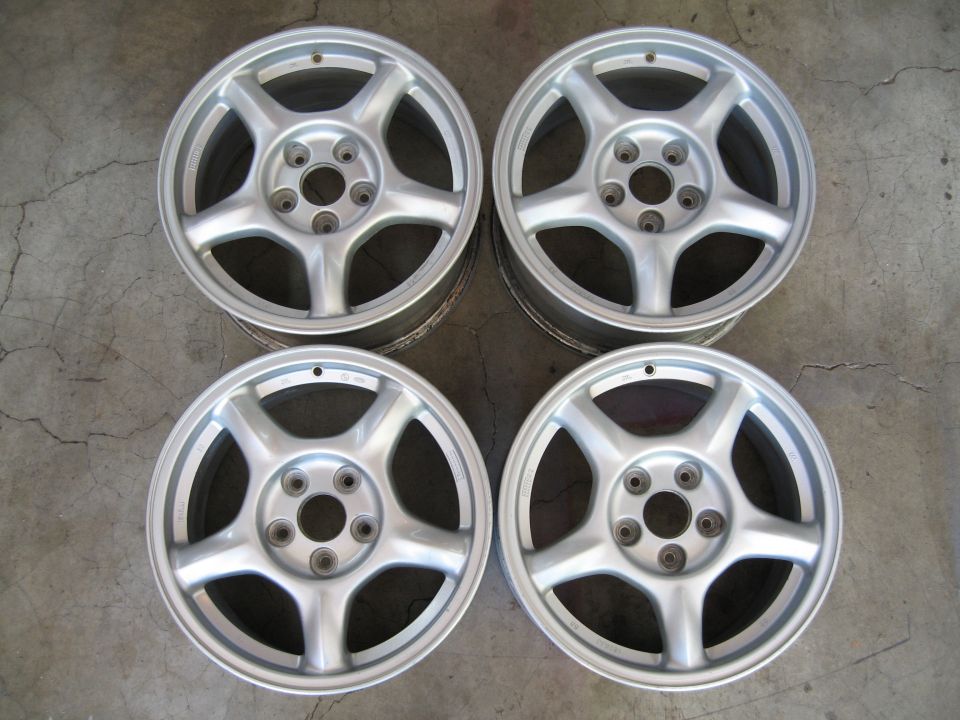 Four silver alloy wheels with five spokes each, arranged on a concrete floor