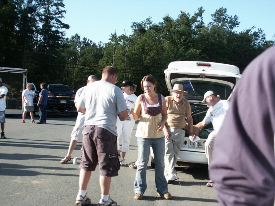 White sedan with open trunk, people gathered around. License plate LV 690