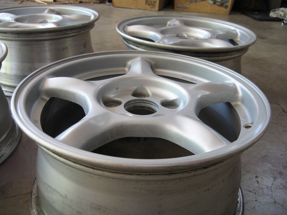 several silver 5-spoke car wheels stacked up