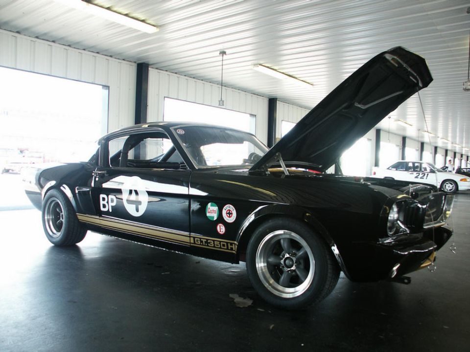 Black 1966 Ford Mustang GT350H race car with hood open, BP and number 4 decals. Another white car visible in background