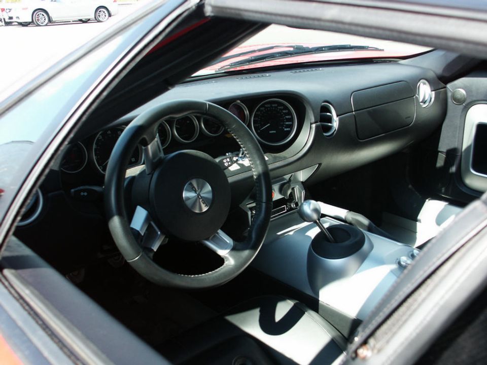 Interior view of a red convertible with a sporty dashboard and shifter. Another white car is visible outside