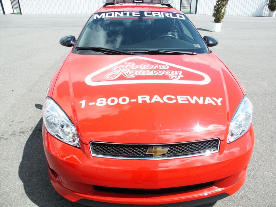 Red Chevrolet Monte Carlo with 'MONTE CARLO' windshield banner and 'Pocono Raceway' decal