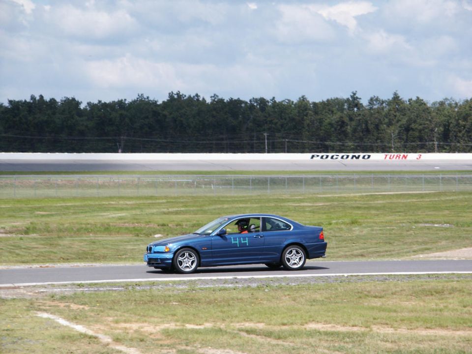 Blue coupe with number 44 on the door driving on a racetrack. Pocono Turn 3 sign visible
