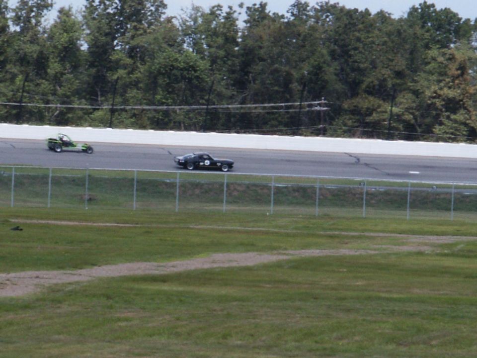 Black race car and green go-kart on a track, trees in background