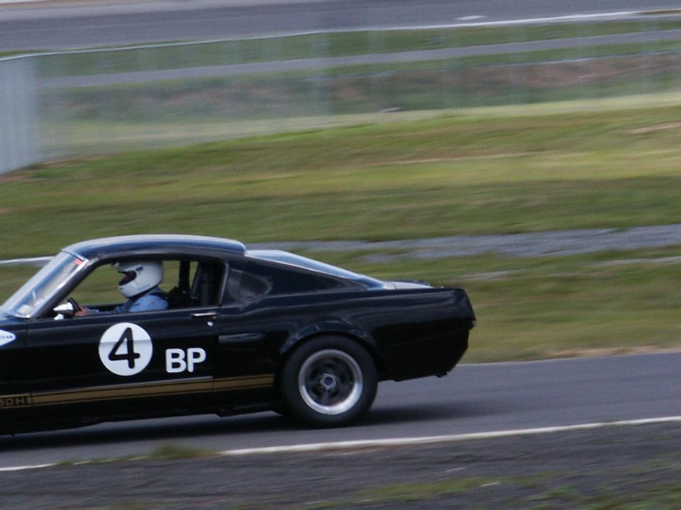Black 1968 Ford Mustang race car with gold stripe and number 4 BP on the side, seen from the side on a race track