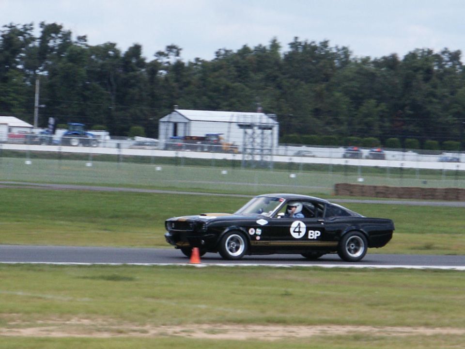 Black 1967 Shelby GT500 on a race track, side view. Gold stripe and number 4 on door