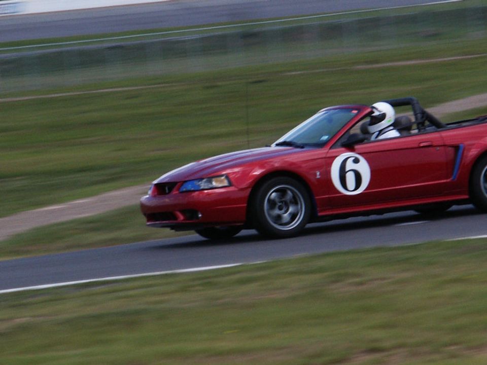 Red convertible race car with number 6 on its side, driver wearing a helmet, on a race track