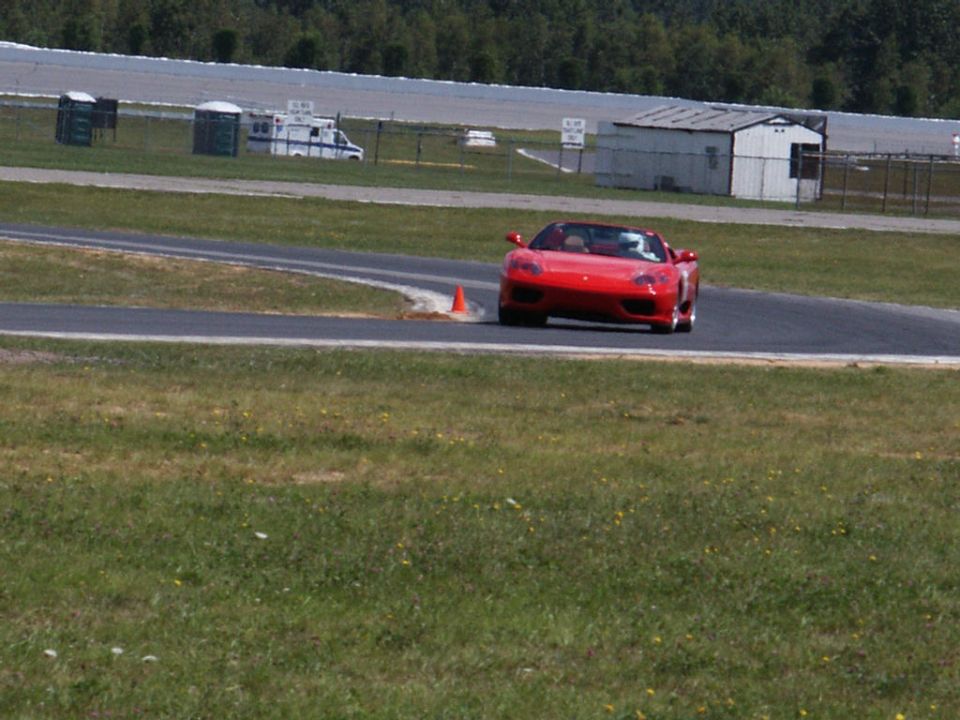 Red convertible sports car on a race track with an ambulance and portable toilets in the background