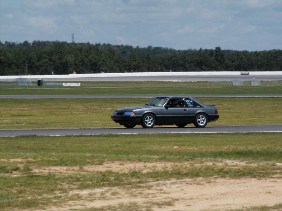 Dark gray coupe with racing number 54 on the door, driving on a race track
