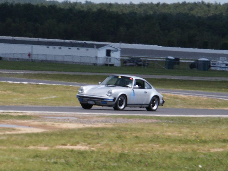 Silver Porsche 911 on a racetrack, front 3/4 view. Blue stripe on door