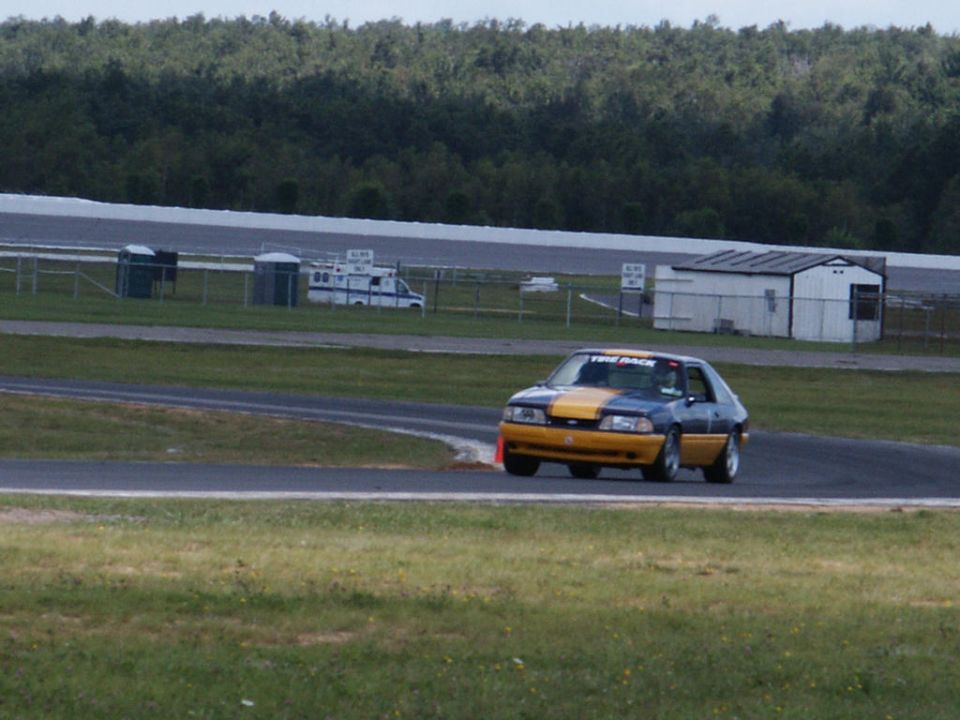 Blue and yellow coupe on race track with 'TIRE RACK' sticker on windshield