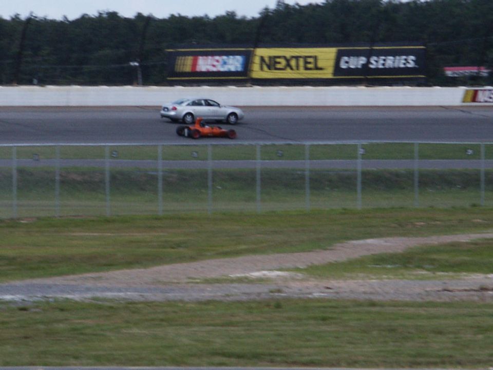Silver sedan and orange race car on a race track with NASCAR Nextel Cup Series banner