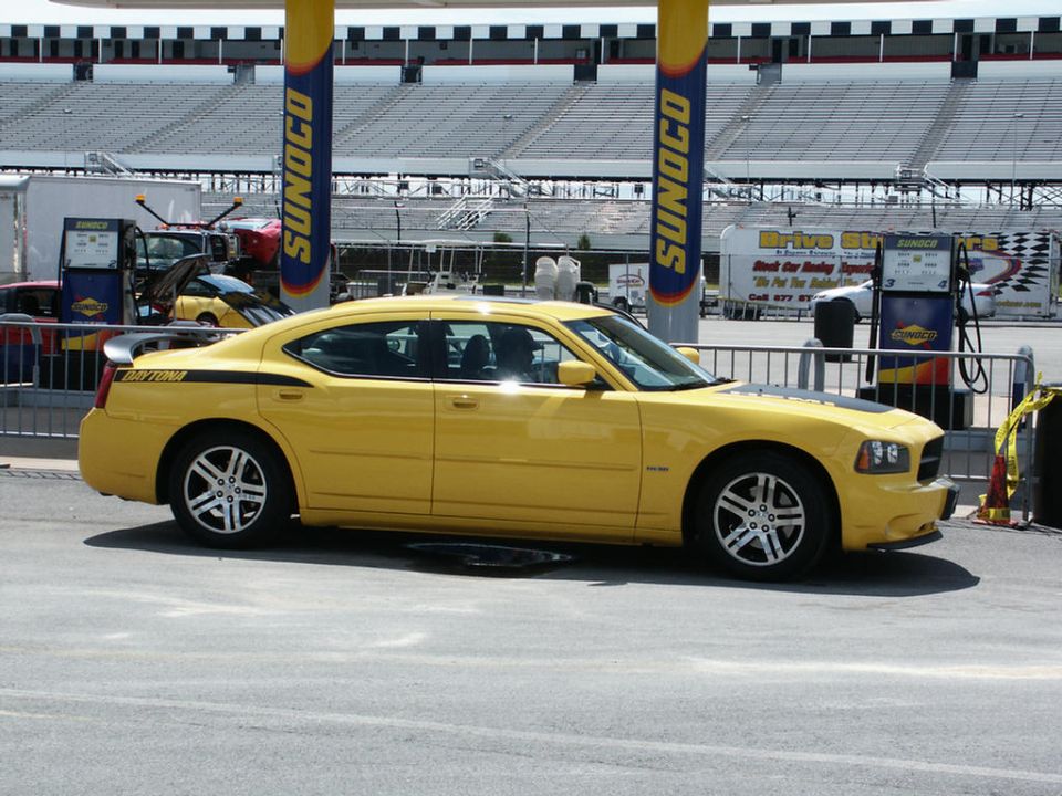 Yellow Dodge Charger Daytona with black stripe on side, parked at a gas station at a racetrack