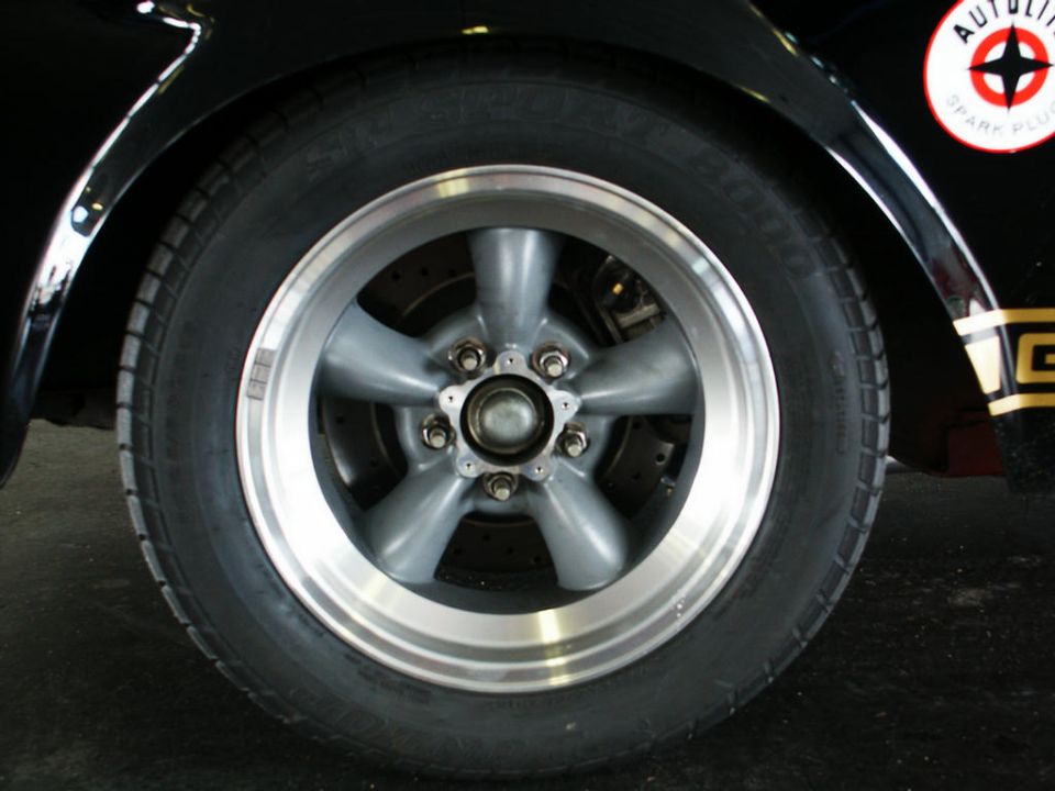 Close-up of a five-spoke aftermarket wheel and tire on a black car, with an Autolite Spark Plugs sticker visible