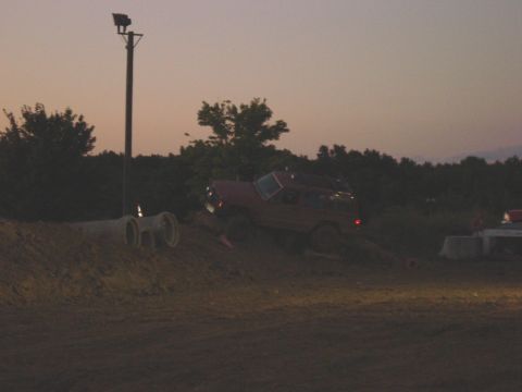 1994 Ford Bronco - A red SUV navigates a dirt obstacle course at dusk.