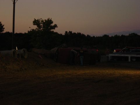 1994 Ford Bronco - An overturned vehicle lies on a dirt mound as another vehicle is parked nearby during twilight.