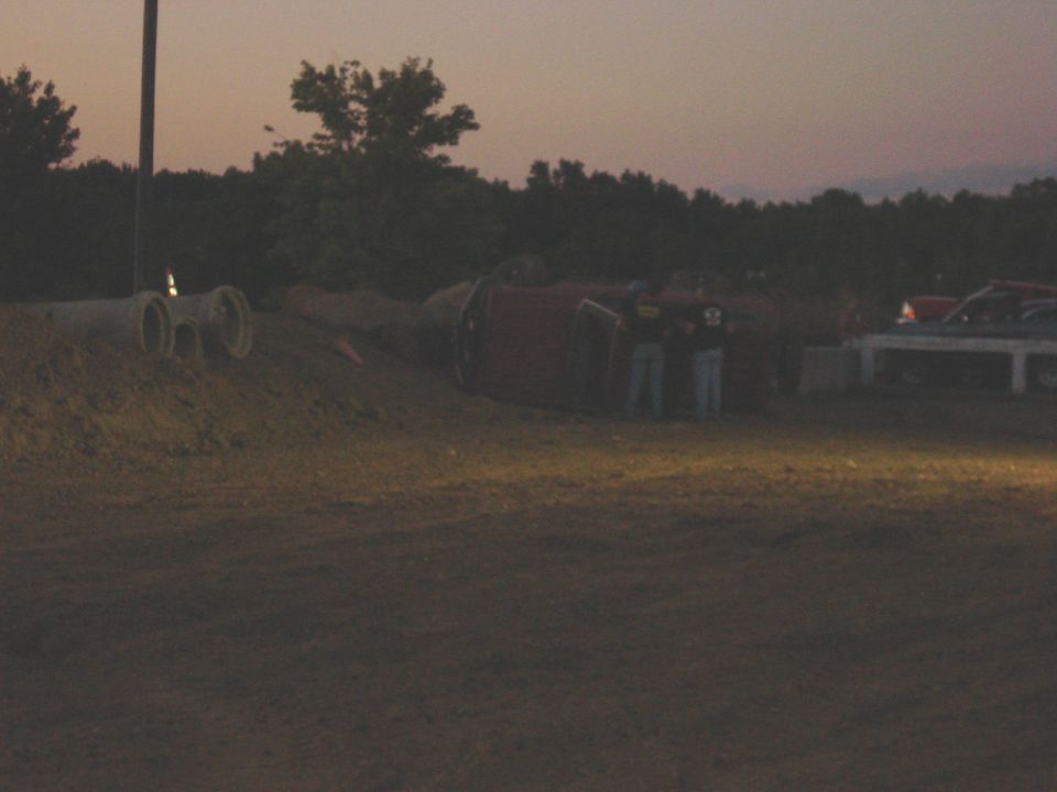 red vehicle on its side near some concrete pipes, two people standing nearby