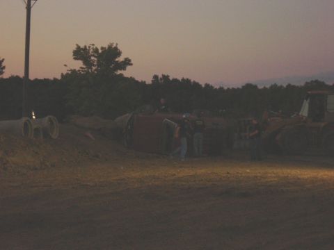 1994 Ford Bronco - A red SUV has rolled onto its side, with several people observing the scene and a bulldozer nearby.