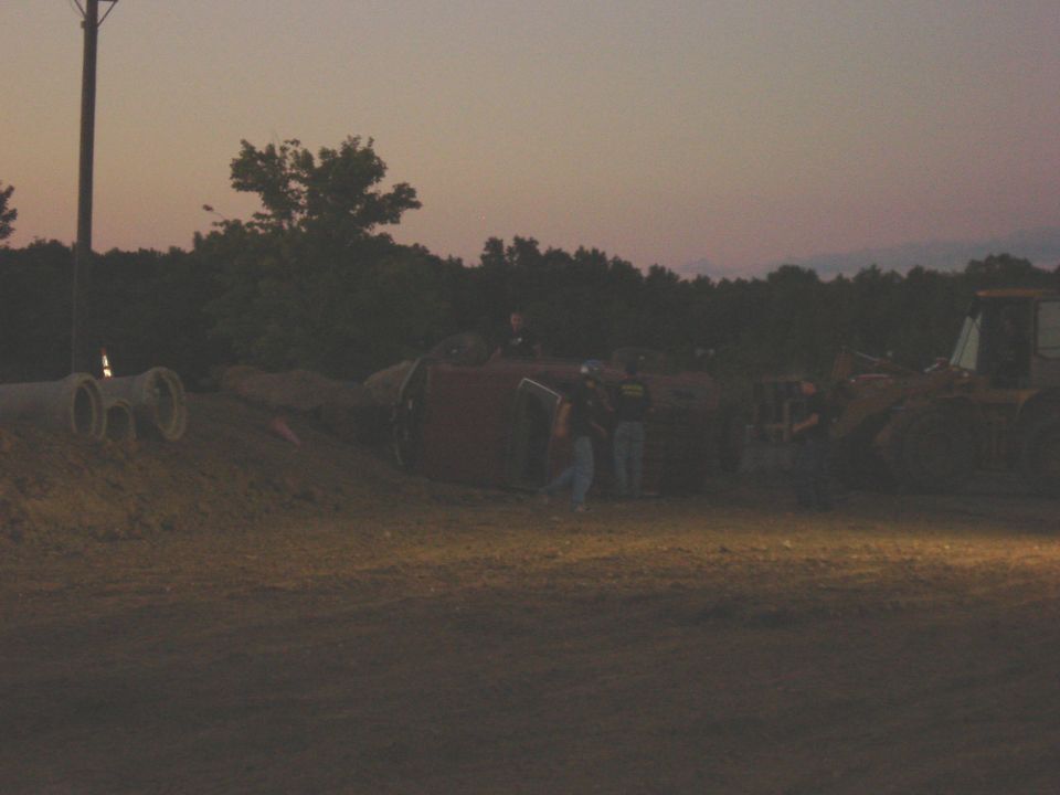 Red SUV on its side with people around it and a bulldozer in the background