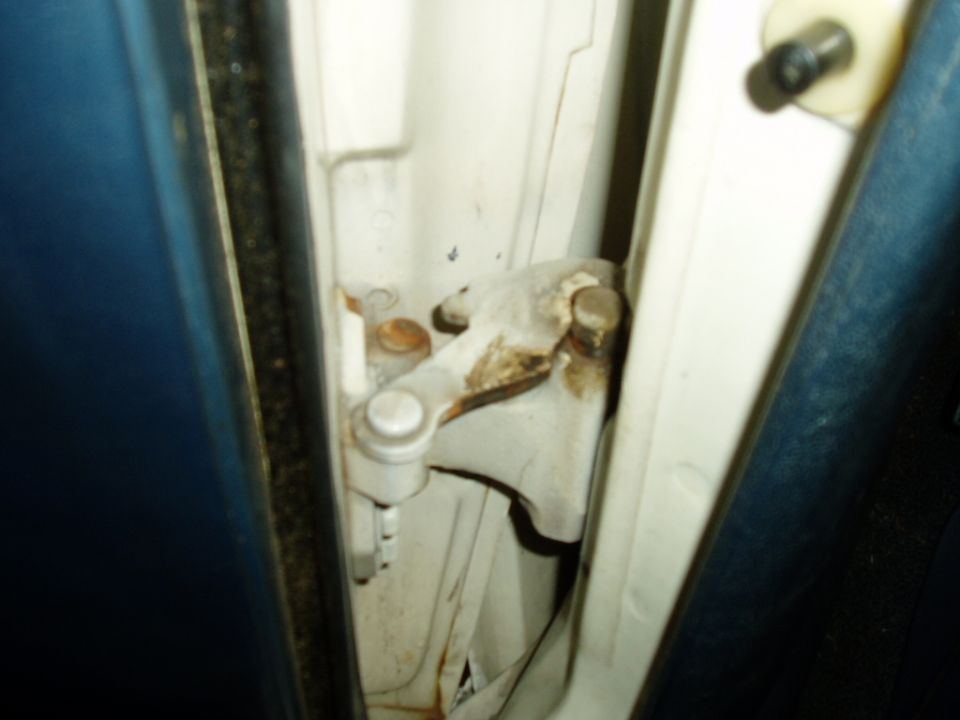 Close-up of a car's door hinge mechanism, showing metal parts and some rust