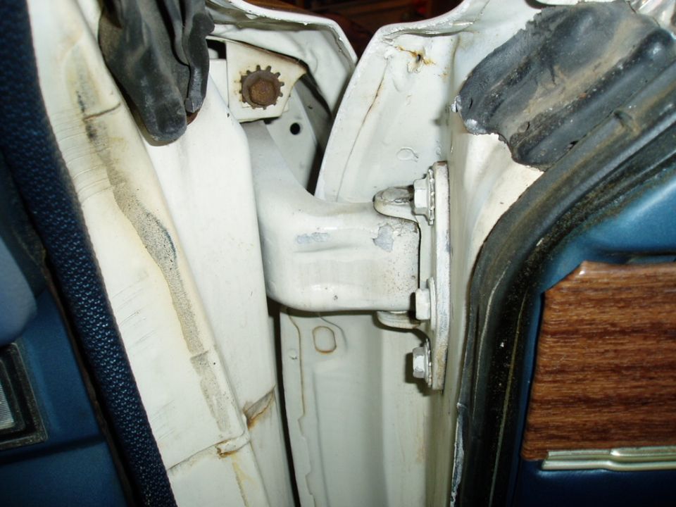 White door jamb with visible rust and a door hinge mechanism. Blue interior trim with wood grain is partially visible