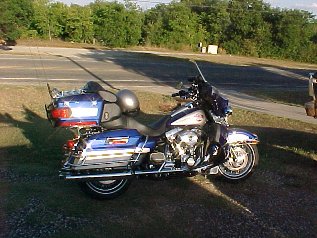 Blue and silver Harley-Davidson motorcycle parked on gravel near a road