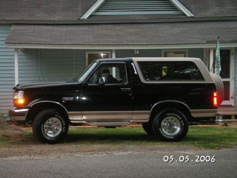 1996 Ford Bronco - A black and tan Ford Bronco is parked on a gravel driveway in front of a light blue house.