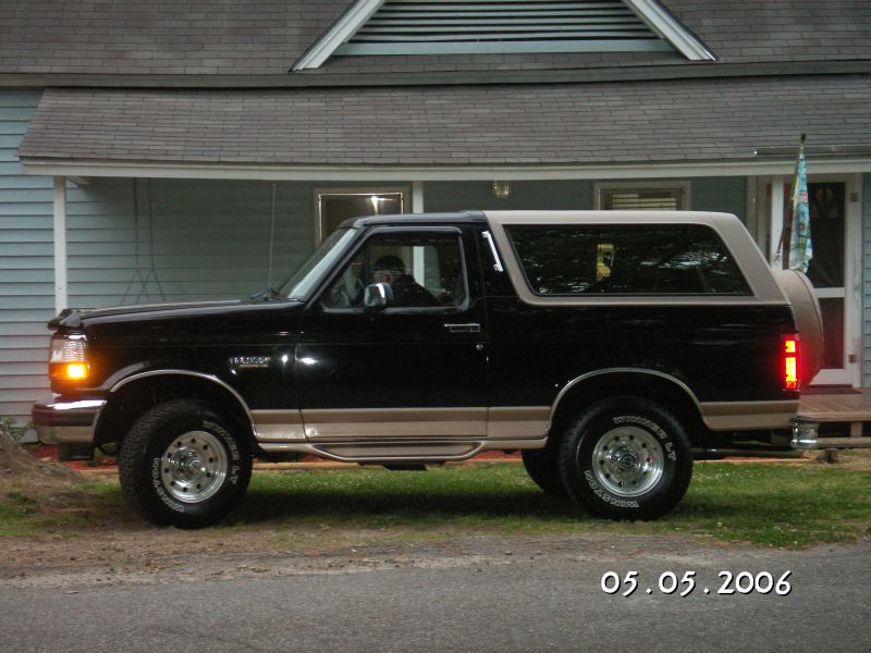 Black Ford Bronco with tan trim, side view, parked in front of a house