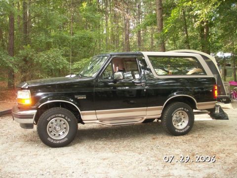1996 Ford Bronco - This is a side view of a black Ford Bronco with tan trim, parked outdoors.