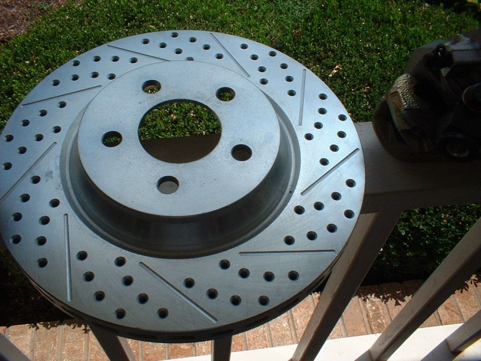 Slotted and drilled brake rotor with caliper, part of a braking system