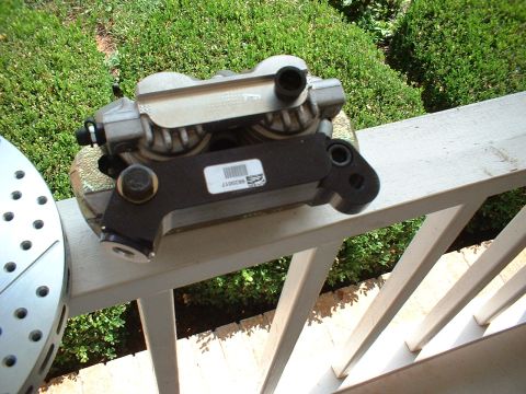 1969 Ford Mustang - A brake caliper and slotted rotor are shown resting on a white railing outdoors.