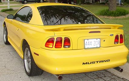 1998 Ford Mustang - Rear view of a yellow 1998 Ford Mustang coupe with a spoiler and a custom license plate.