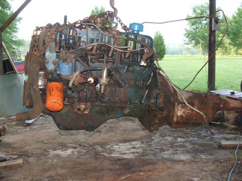 1972 Ford Ranchero - A heavily rusted engine and transmission assembly hangs from a chain hoist outdoors.