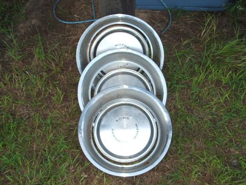 1966 Ford Ranchero - Three Ford hubcaps are stacked on the ground, showing visible text including 'MOTOR' and 'FORD'.