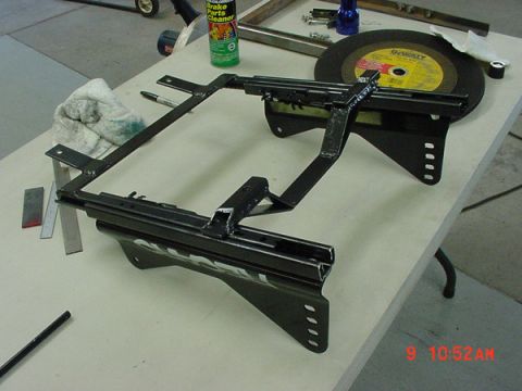 1993 Ford Mustang - A car seat bracket assembly is shown on a workbench with various tools and a can of brake parts cleaner.