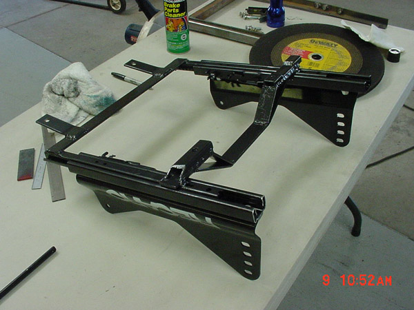 Black metal car seat bracket assembly on a table with tools