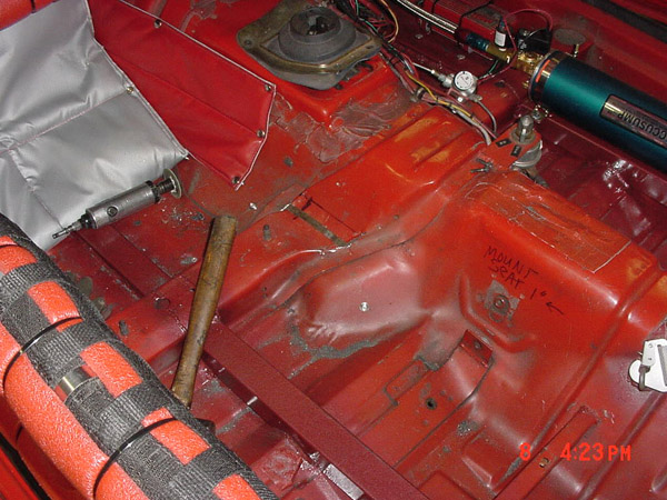 Car interior floor stripped bare, showing red paint, tools, and a green air suspension tank