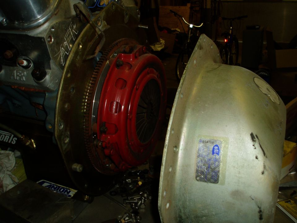 Engine clutch assembly with red pressure plate and silver housing, next to a metal shield with a sticker