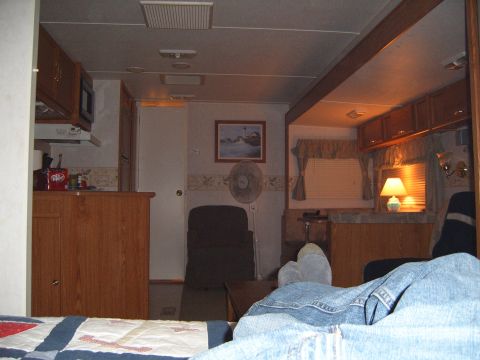 1993 Ford Bronco - The interior of a camper shows a kitchen area, a seating area with a fan and picture on the wall, and a bed in the foreground.