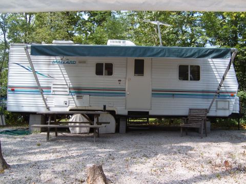 1993 Ford Bronco - A Mallard travel trailer is parked on a gravel surface, surrounded by trees.