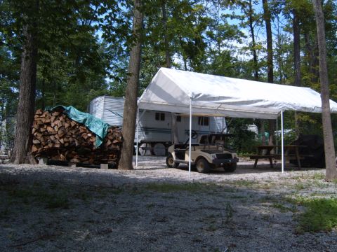 1993 Ford Bronco - A golf cart sits under a white canopy at a campsite, with an RV and stacked firewood nearby.