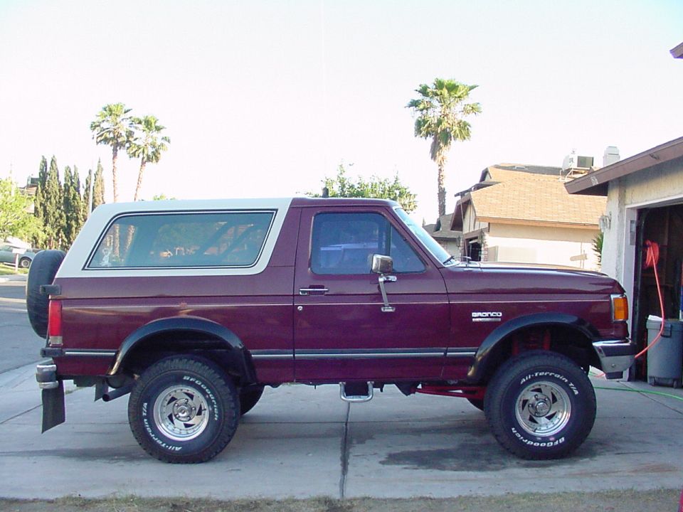 Side view of lifted maroon Ford Bronco with white top and BFGoodrich All-Terrain tires in a driveway