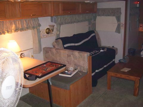 1993 Ford Bronco - The interior of a camper shows a dinette table, a couch with a blanket, and a fan.